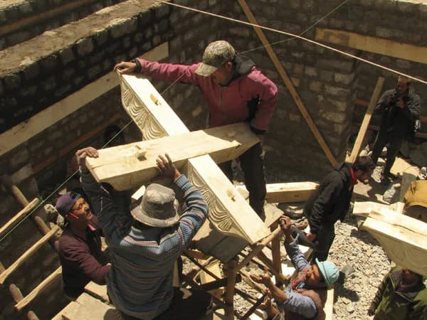 Ladakhi carpenters lifting a carved timber beam into place inside the tower's stone walls